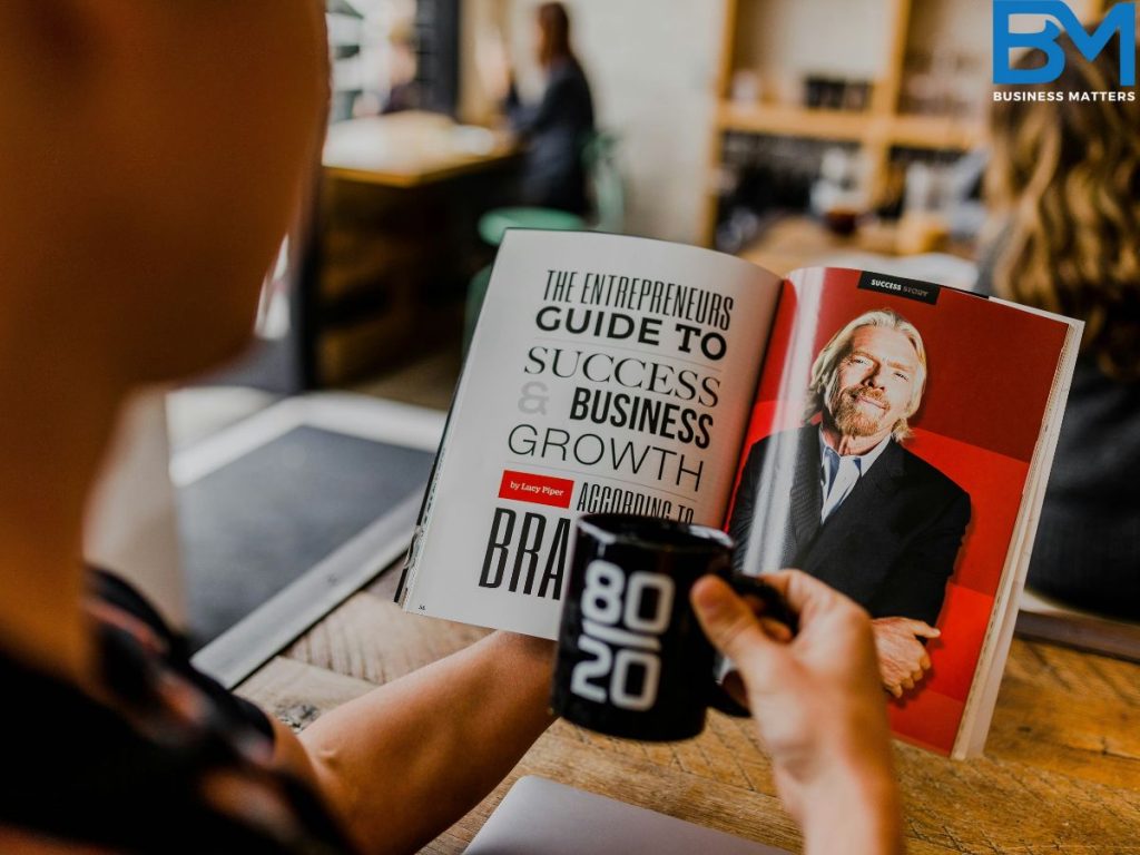 business magazine in the hand of an individual with a coffee mug and the image of Richard Branson in the business magazine